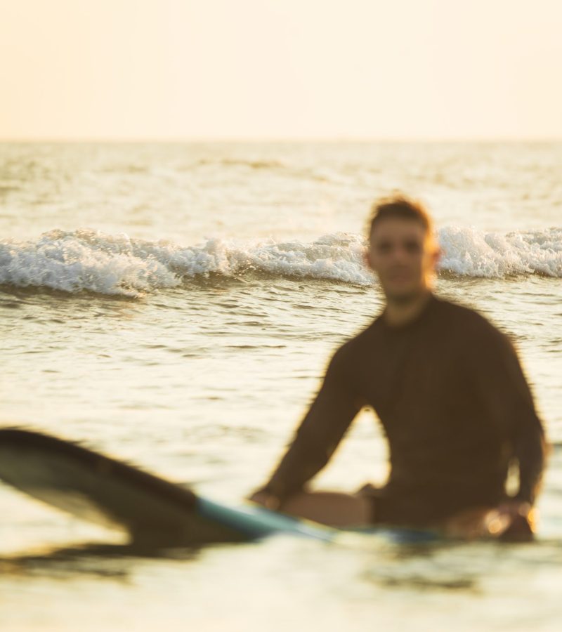 Out-of-focus surfer resting on his surfboard in the ocean.